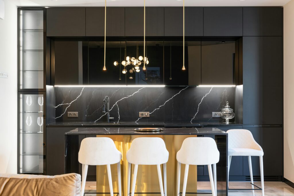 A stylish contemporary kitchen with black cabinetry, marble countertop, and chic lighting.